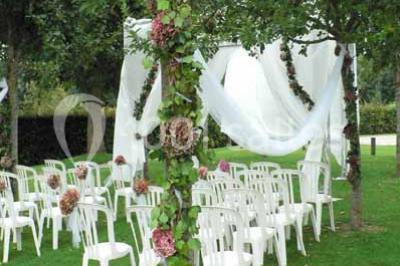 Un bâtiment en pierre avec un toit en tuiles rouges, entouré de jardins fleuris, accueille un groupe de personnes.