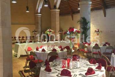 Un bâtiment en pierre avec un toit en tuiles rouges, entouré de jardins fleuris, accueille un groupe de personnes.