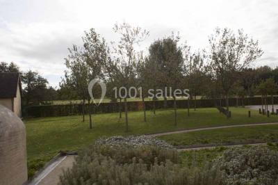 Un bâtiment en pierre avec un toit en tuiles rouges, entouré de jardins fleuris, accueille un groupe de personnes.