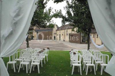 Un bâtiment en pierre avec un toit en tuiles rouges, entouré de jardins fleuris, accueille un groupe de personnes.