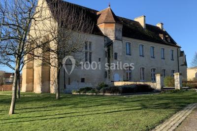 Un bâtiment en pierre avec un toit en tuiles rouges, entouré de jardins fleuris, accueille un groupe de personnes.