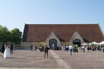 Un bâtiment en pierre avec un toit en tuiles rouges, entouré de jardins fleuris, accueille un groupe de personnes.