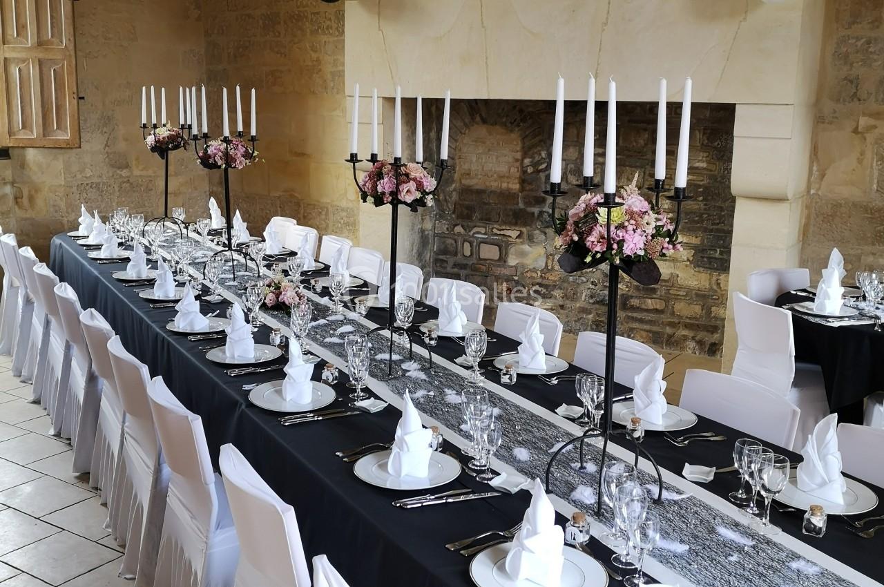 Grande table de réception élégamment dressée avec nappes noires, chandeliers, fleurs et serviettes pliées, dans une salle en…