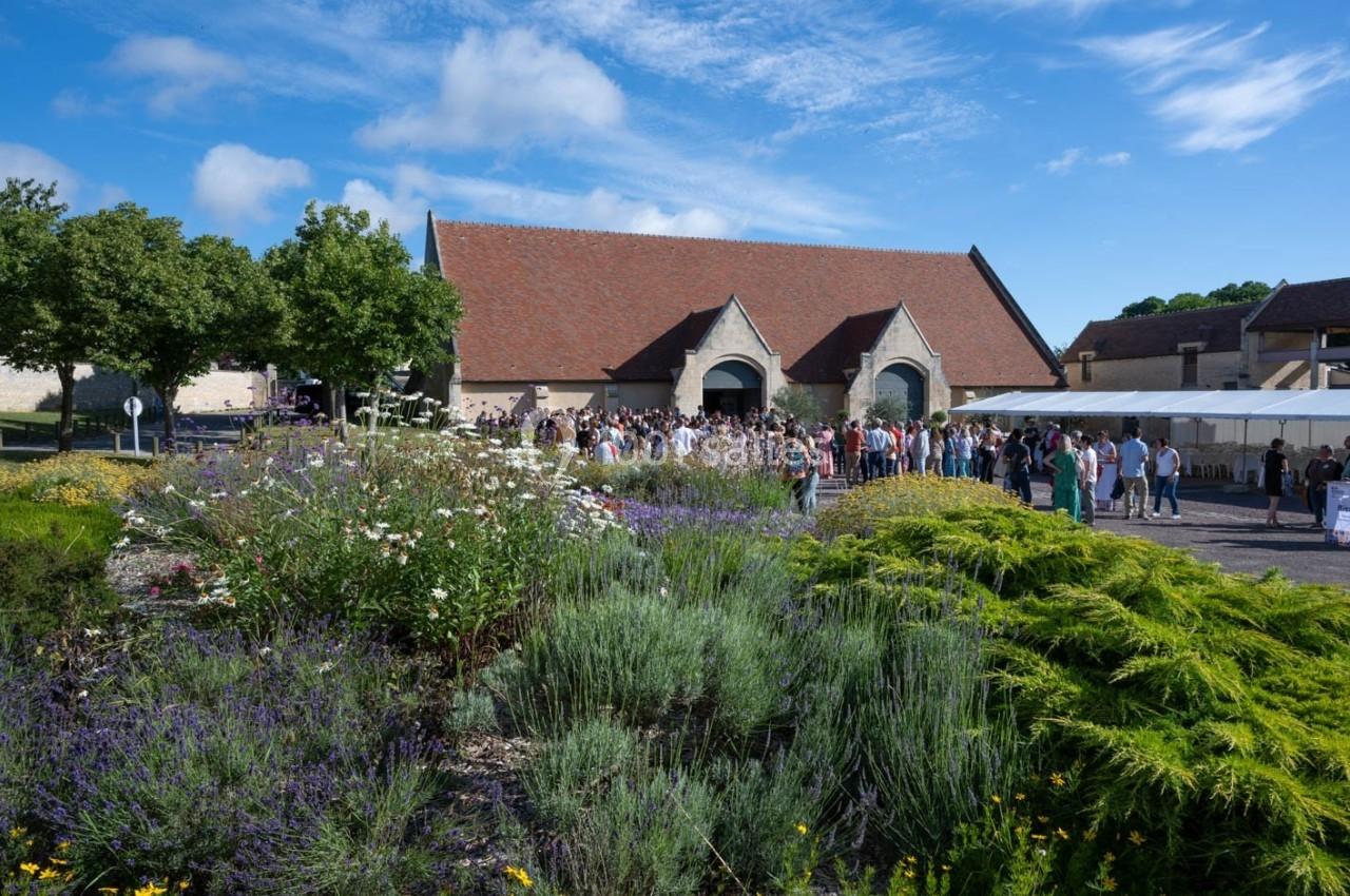 Un bâtiment en pierre avec un toit en tuiles rouges, entouré de jardins fleuris, accueille un groupe de personnes.