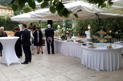 Buffet en extérieur avec tables garnies de plats, invités debout discutant sous des parasols blancs.
