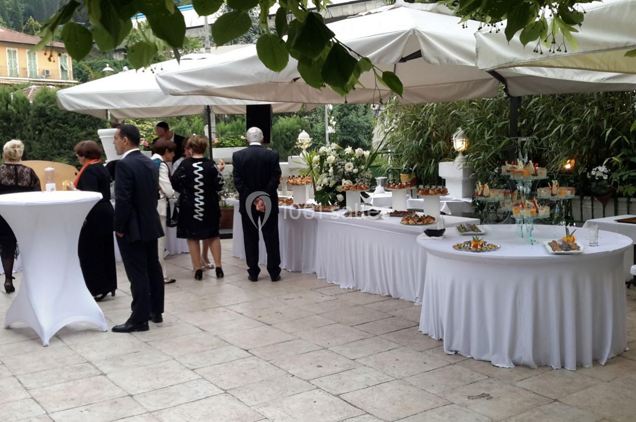 Buffet en extérieur avec tables garnies de plats, invités debout discutant sous des parasols blancs.