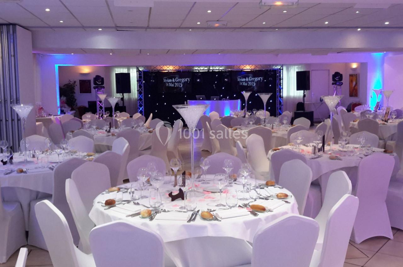 Salle de réception décorée avec des tables rondes dressées, nappes blanches et éclairage d'ambiance violet.