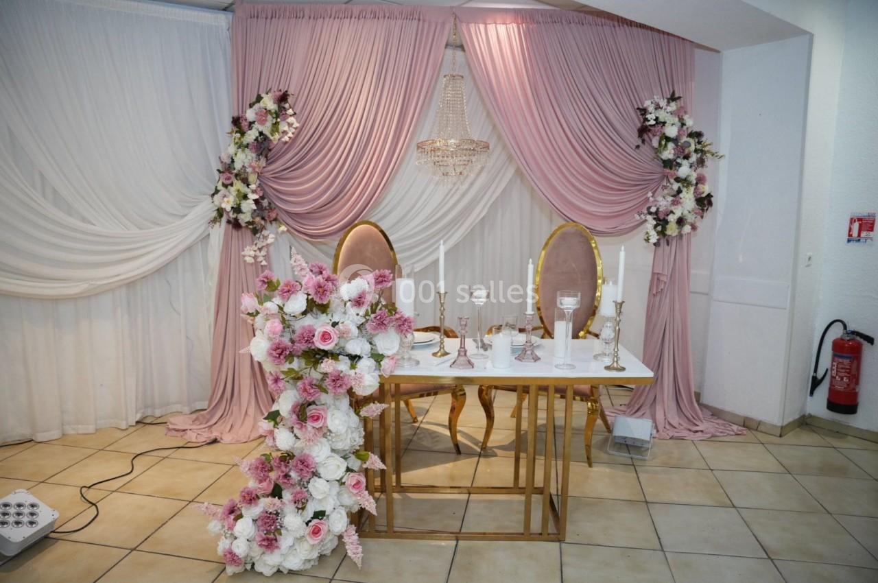 Décoration de table de mariage avec chaises dorées, fleurs roses et blanches, et rideaux drapés roses et blancs.