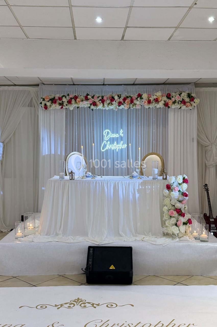 Table d'honneur décorée de fleurs, bougies et miroirs, dans une salle de réception avec rideaux blancs.