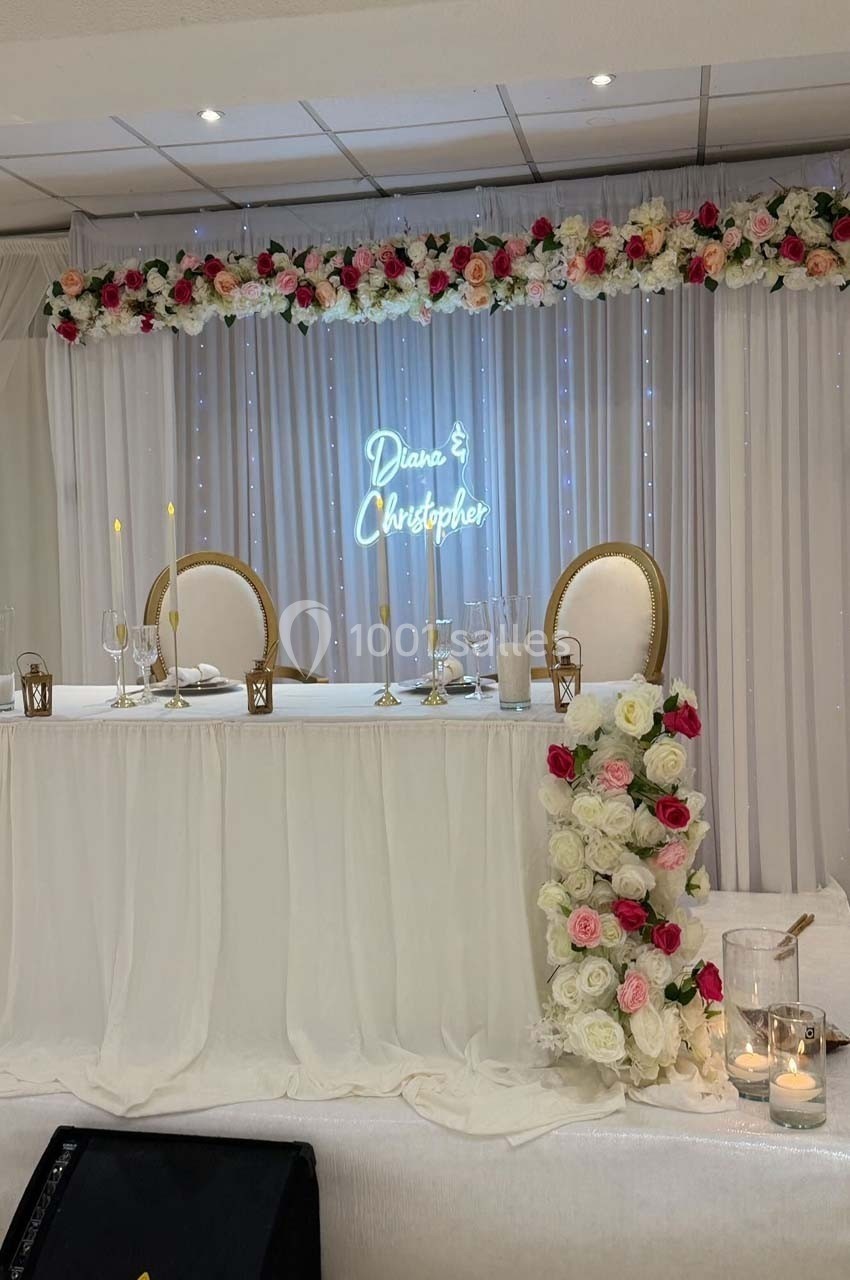 Table d'honneur décorée de fleurs blanches et roses, avec un panneau lumineux affichant des prénoms en arrière-plan.