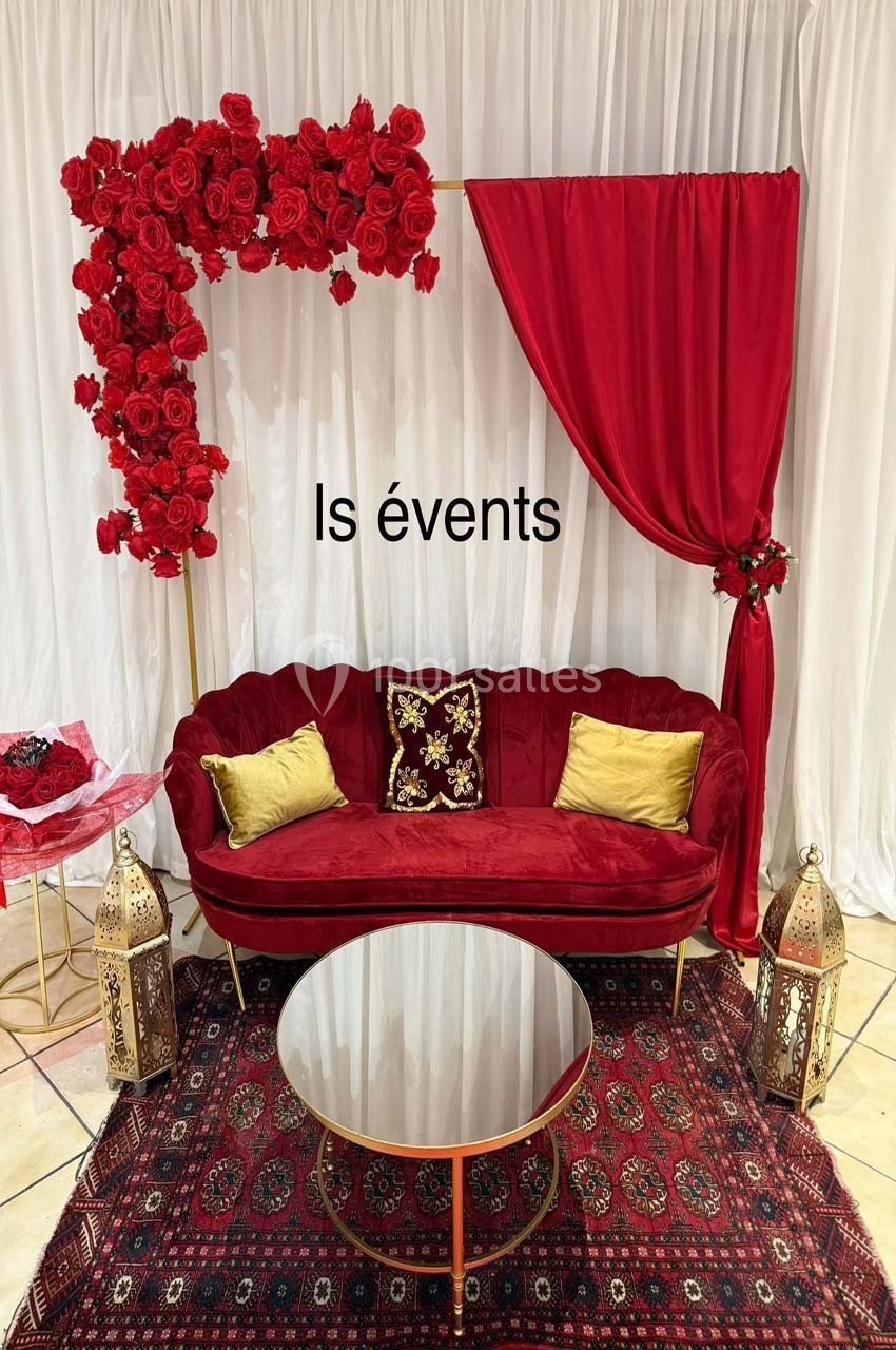 Canapé rouge avec coussins dorés, table basse ronde, lanternes dorées et décorations de roses rouges sur fond de rideaux…