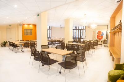 Salle de réunion lumineuse avec tables alignées, chaises noires, bouteilles d'eau et étagères en arrière-plan.