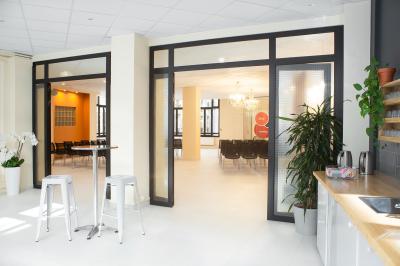 Salle de réunion lumineuse avec tables alignées, chaises noires, bouteilles d'eau et étagères en arrière-plan.