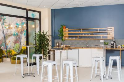 Salle de réunion lumineuse avec tables alignées, chaises noires, bouteilles d'eau et étagères en arrière-plan.