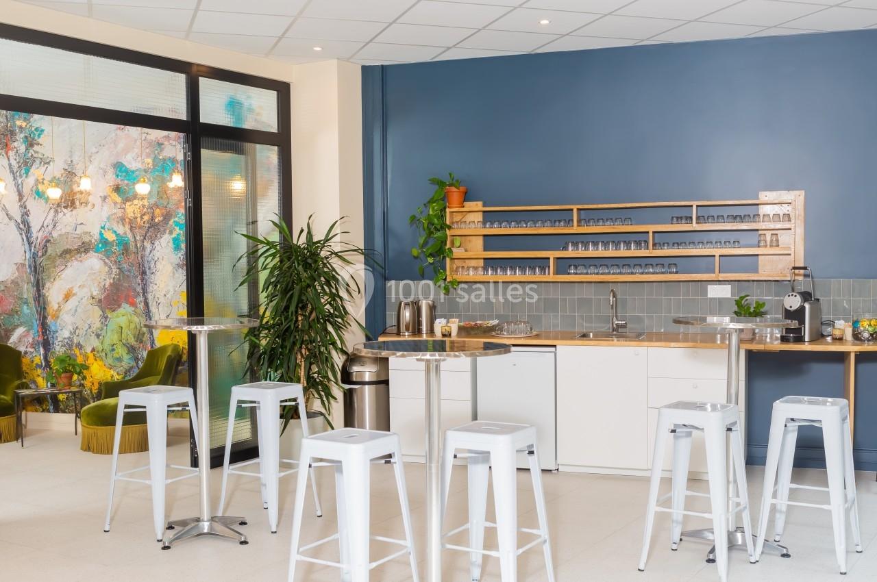 Cuisine moderne avec comptoir, tabourets hauts blancs, étagères en bois, plantes et mur bleu en arrière-plan.