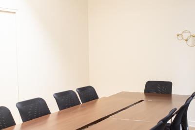 Salle de réunion lumineuse avec tables alignées, chaises noires, bouteilles d'eau et étagères en arrière-plan.