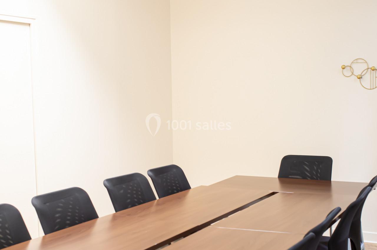 Salle de réunion lumineuse avec une grande table en bois, des chaises noires et un projecteur fixé au plafond.