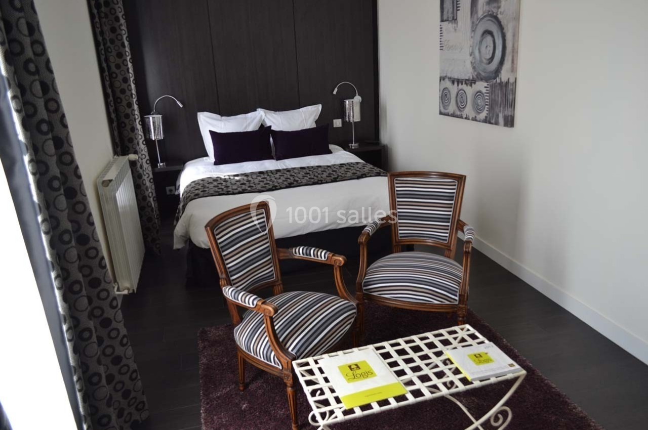 Chambre avec lit double, deux fauteuils rayés, table basse blanche et décoration murale dans un intérieur moderne.