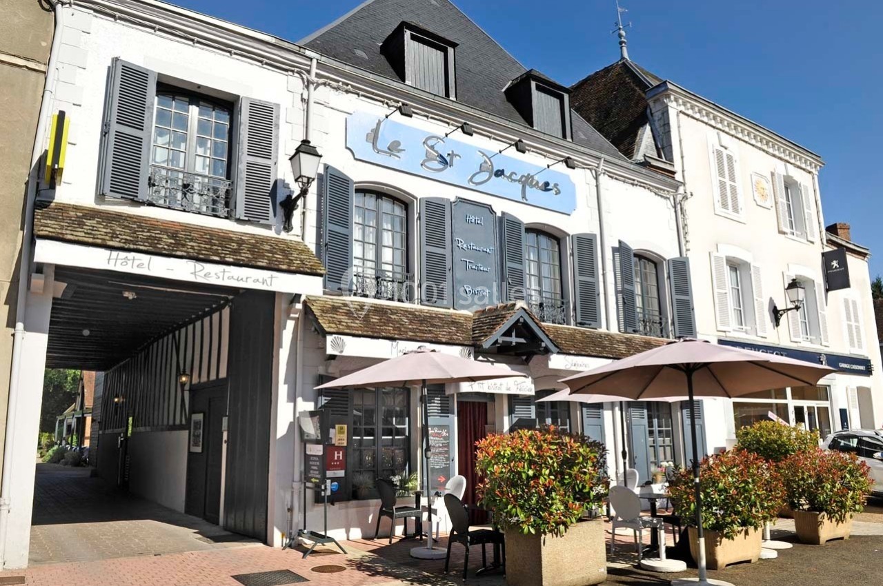 Façade d'un hôtel-restaurant avec terrasse, parasols et plantes, situé dans un bâtiment traditionnel.