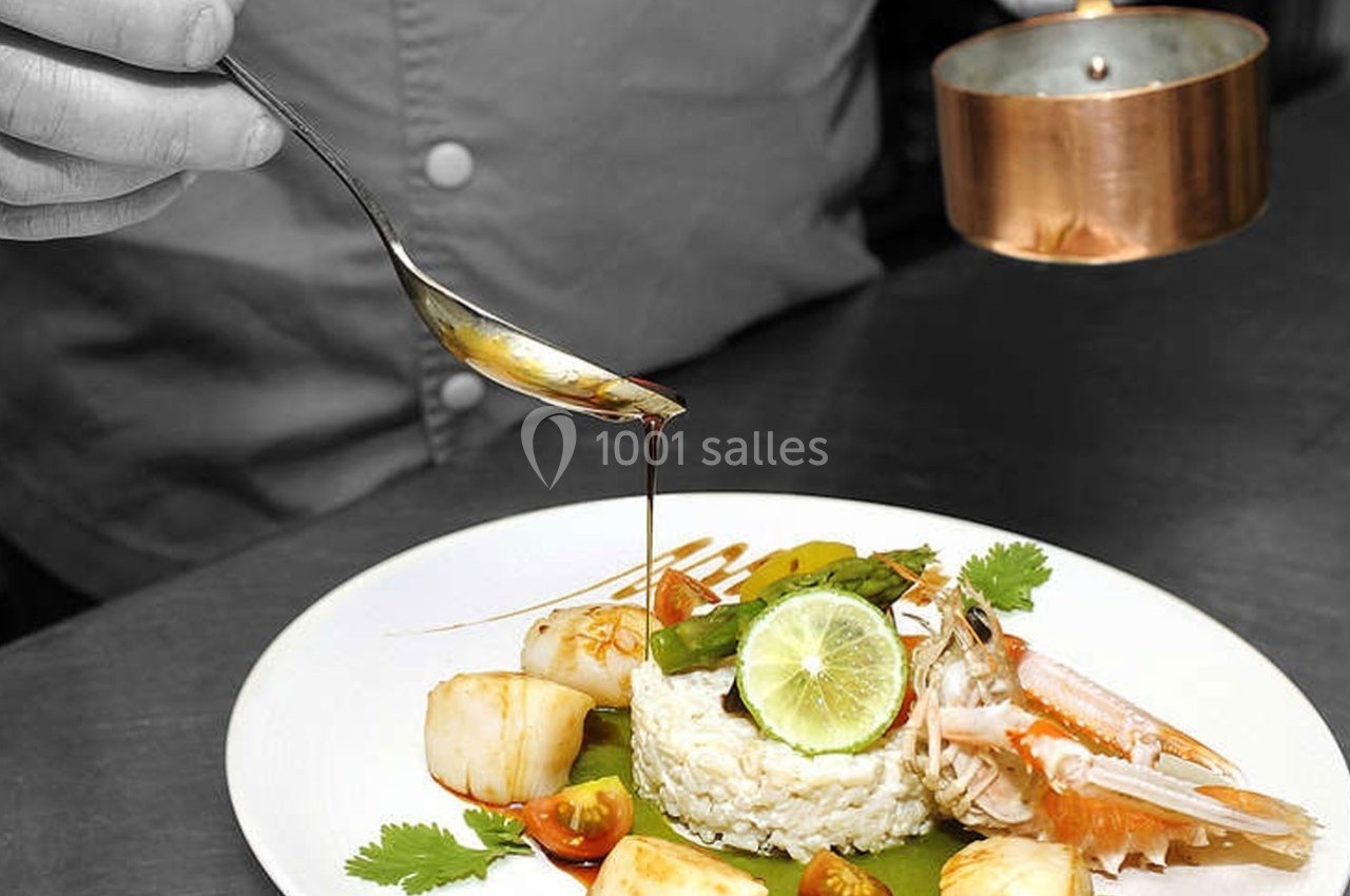 Un chef verse une sauce sur un plat raffiné composé de riz, fruits de mer, légumes et citron vert.