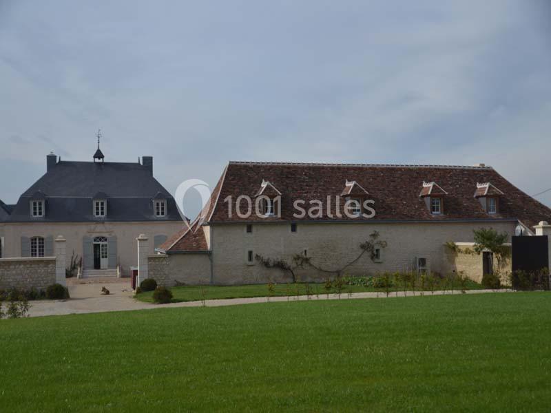 Bâtiments en pierre avec toits en ardoise et tuiles, entourés de pelouse et d'un ciel dégagé.
