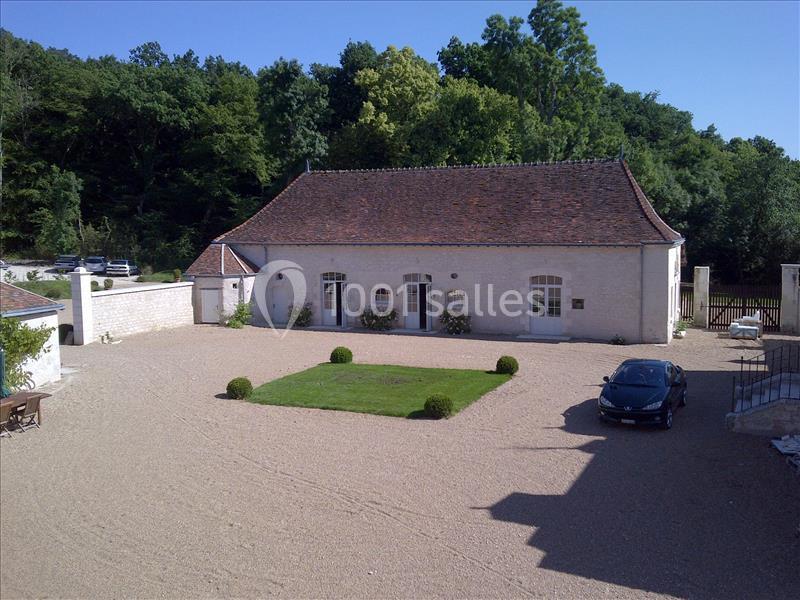 Cour d'une propriété avec une maison en pierre, toit en tuiles, pelouse centrale et une voiture garée à droite.