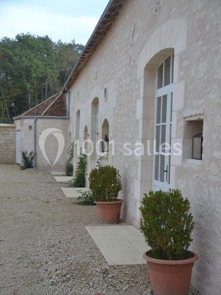 Façade en pierre d'un bâtiment avec des portes vitrées et des pots de buis alignés sur une allée gravillonnée.