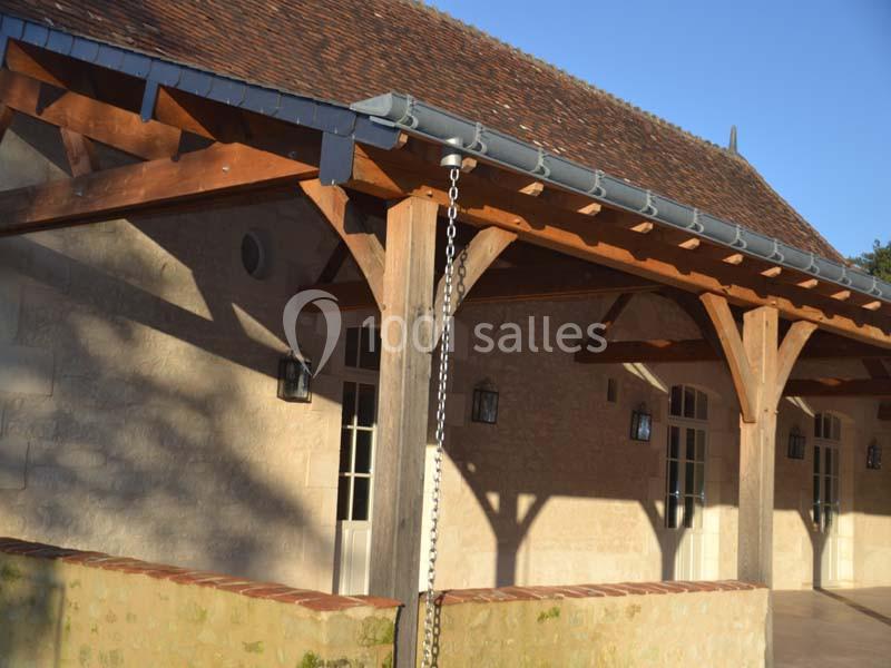 Façade d'un bâtiment en pierre avec toit en tuiles, poutres en bois apparentes et gouttière métallique.