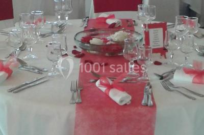 Salle de réception lumineuse avec tables dressées, chaises blanches, chandeliers et décorations florales.