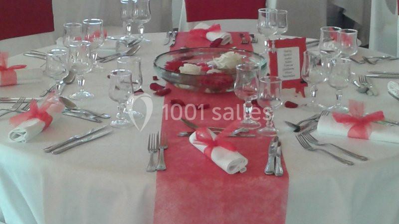 Table dressée avec nappe blanche, chemin de table rose, couverts alignés, serviettes nouées et décoration florale.