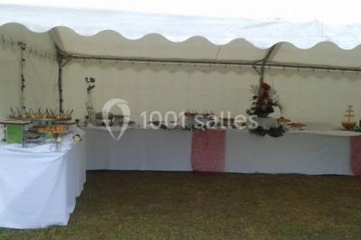 Salle de réception lumineuse avec tables dressées, chaises blanches, chandeliers et décorations florales.