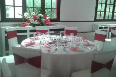 Salle de réception lumineuse avec tables dressées, chaises blanches, chandeliers et décorations florales.