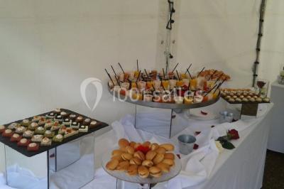 Salle de réception lumineuse avec tables dressées, chaises blanches, chandeliers et décorations florales.