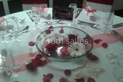 Salle de réception lumineuse avec tables dressées, chaises blanches, chandeliers et décorations florales.