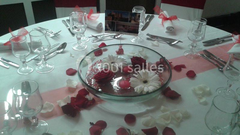 Table dressée avec une nappe blanche, décorée de pétales rouges, d'un centre de table floral et de vaisselle disposée.