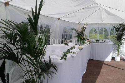 Salle de réception lumineuse avec tables dressées, chaises blanches, chandeliers et décorations florales.