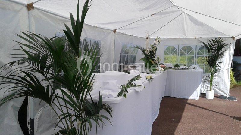 Intérieur d'une tente blanche avec des tables décorées de nappes blanches, de fleurs et de plantes vertes.
