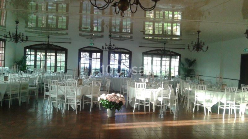 Salle de réception lumineuse avec des tables et chaises blanches, un sol en carrelage et des lustres suspendus.
