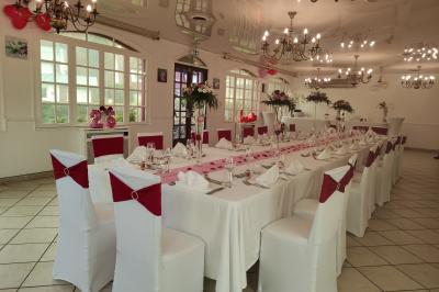Salle de réception lumineuse avec tables dressées, chaises blanches, chandeliers et décorations florales.