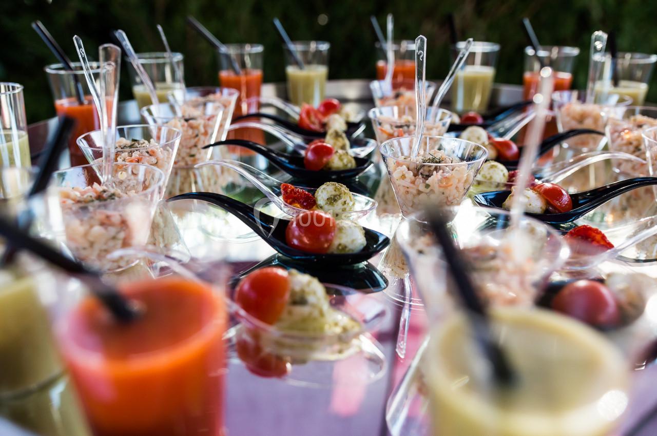 Verrines et cuillères apéritives garnies de légumes, crevettes et sauces, disposées sur une table réfléchissante.