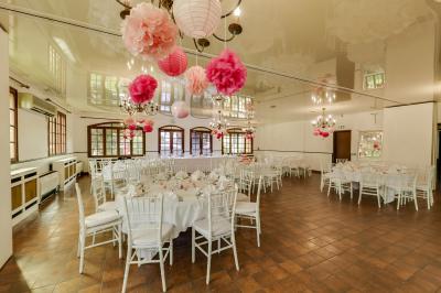 Salle de réception lumineuse avec tables dressées, chaises blanches, chandeliers et décorations florales.