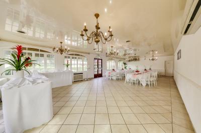 Salle de réception lumineuse avec tables dressées, chaises blanches, chandeliers et décorations florales.
