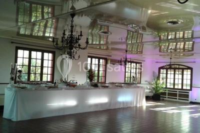 Salle de réception lumineuse avec tables dressées, chaises blanches, chandeliers et décorations florales.