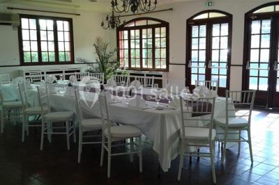 Salle de réception lumineuse avec tables dressées, chaises blanches, chandeliers et décorations florales.