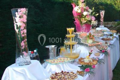 Salle de réception lumineuse avec tables dressées, chaises blanches, chandeliers et décorations florales.