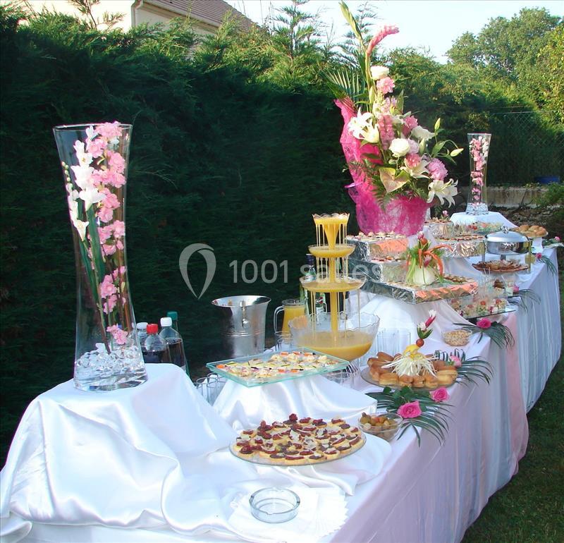 Buffet en extérieur avec nappes blanches, fontaine de jus, plats variés et décorations florales.