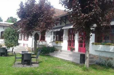 Salle de réception lumineuse avec tables dressées, chaises blanches, chandeliers et décorations florales.