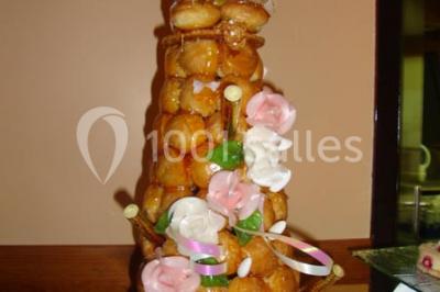Salle de réception lumineuse avec tables dressées, chaises blanches, chandeliers et décorations florales.