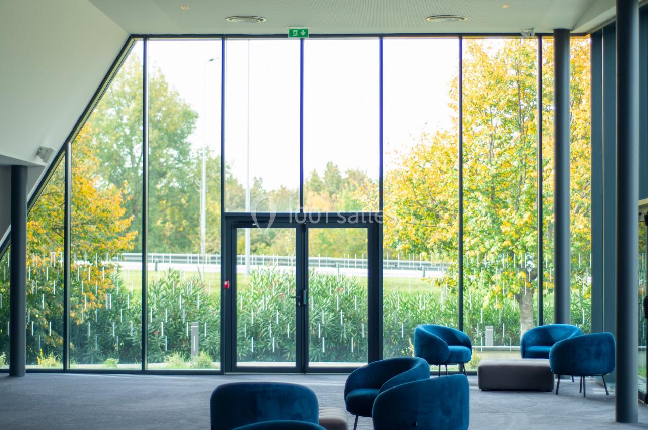 Salle lumineuse avec de grandes baies vitrées, des fauteuils bleus et une vue sur un jardin verdoyant.