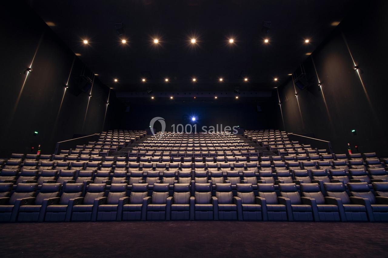Salle de cinéma vide avec rangées de fauteuils alignées et éclairage tamisé au plafond.